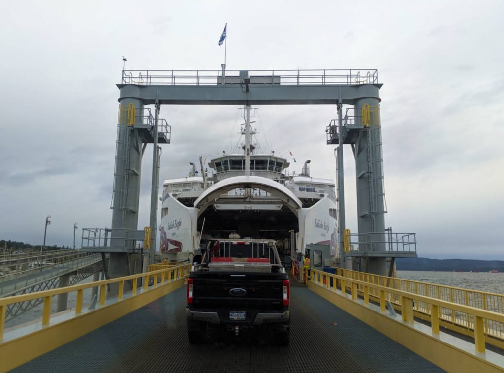 Following a black truck onto vehicle ferry with yellow barriers and peek through ocean views