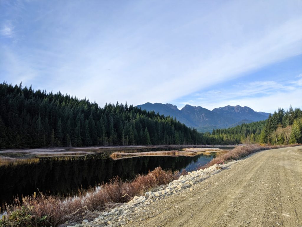 Gravel road next to pond/lake area, with mountain in background