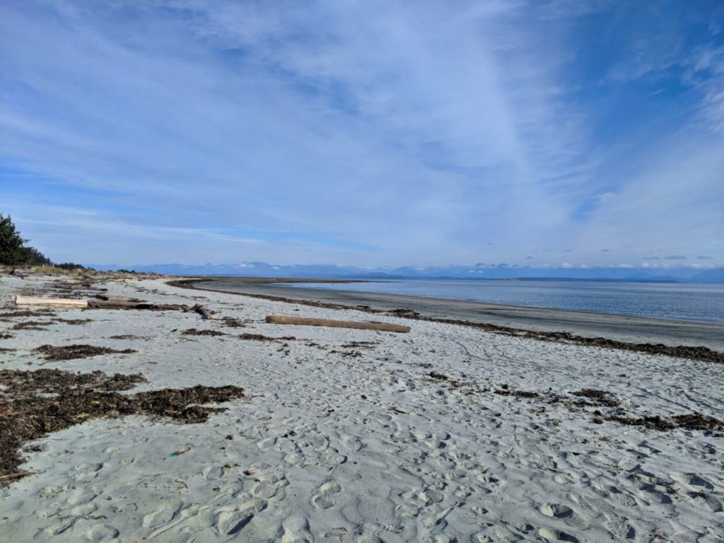 Beach view with white sand and calm ocean, snow capped mountains across the water