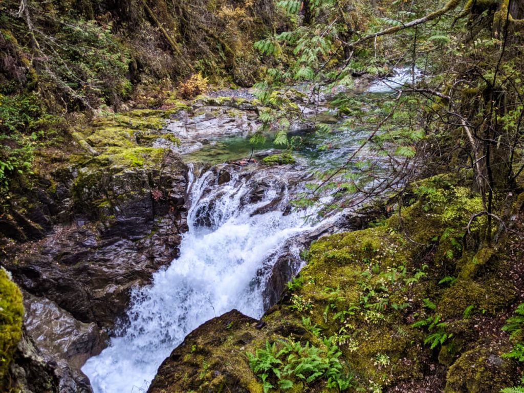 Side view of short waterfall rushing into canyon, surrounded by moss and wet rock