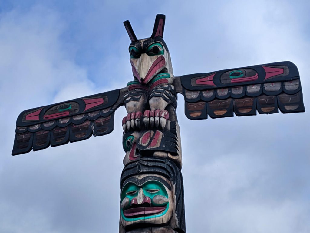 The top of a red, green, black and natural totem pole with a raven's head
