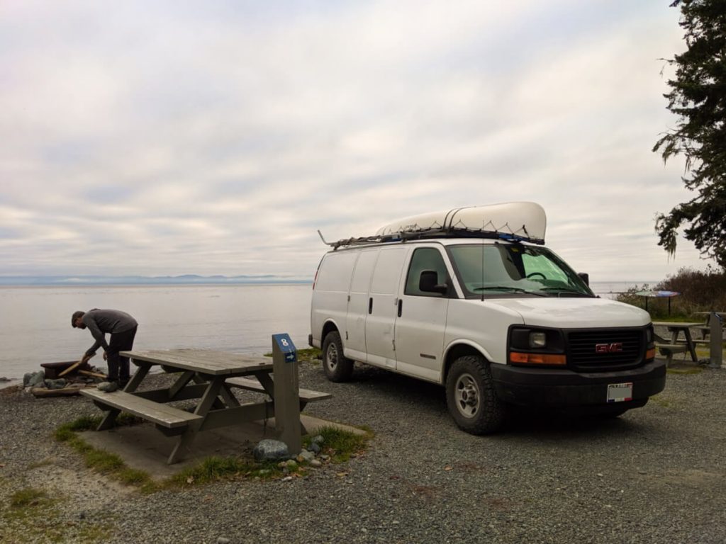 A van is parked next to a picnic table at Jordan River campground, with the doors open