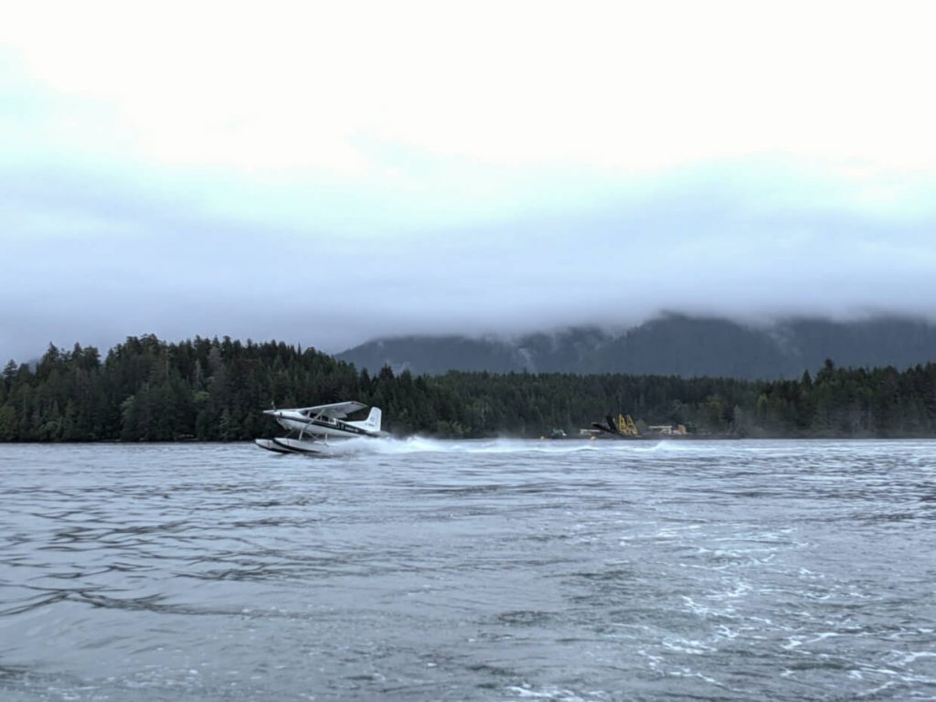 Seaplane taking off in Tofino harbour with backdrop of forest and misty mountains